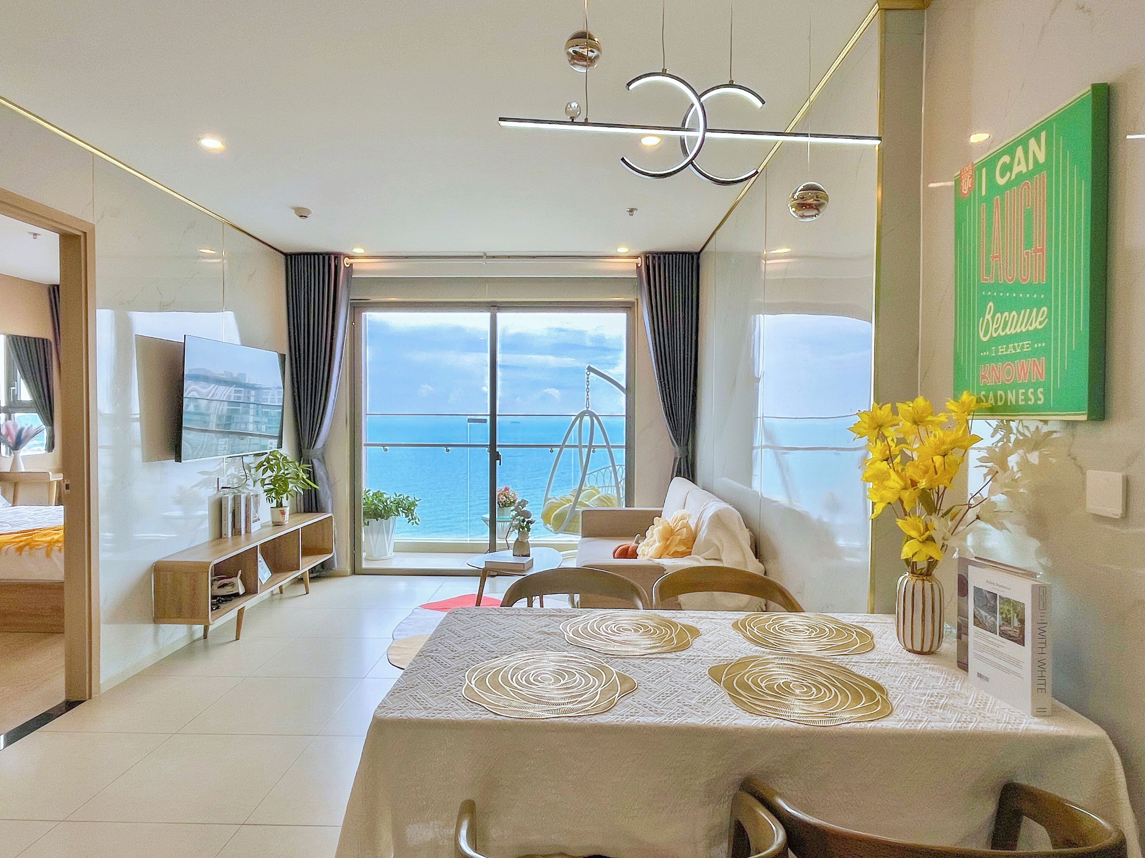 A modern dining area with a table set for four, a balcony with a view of the sea, and a motivational quote on the wall.
