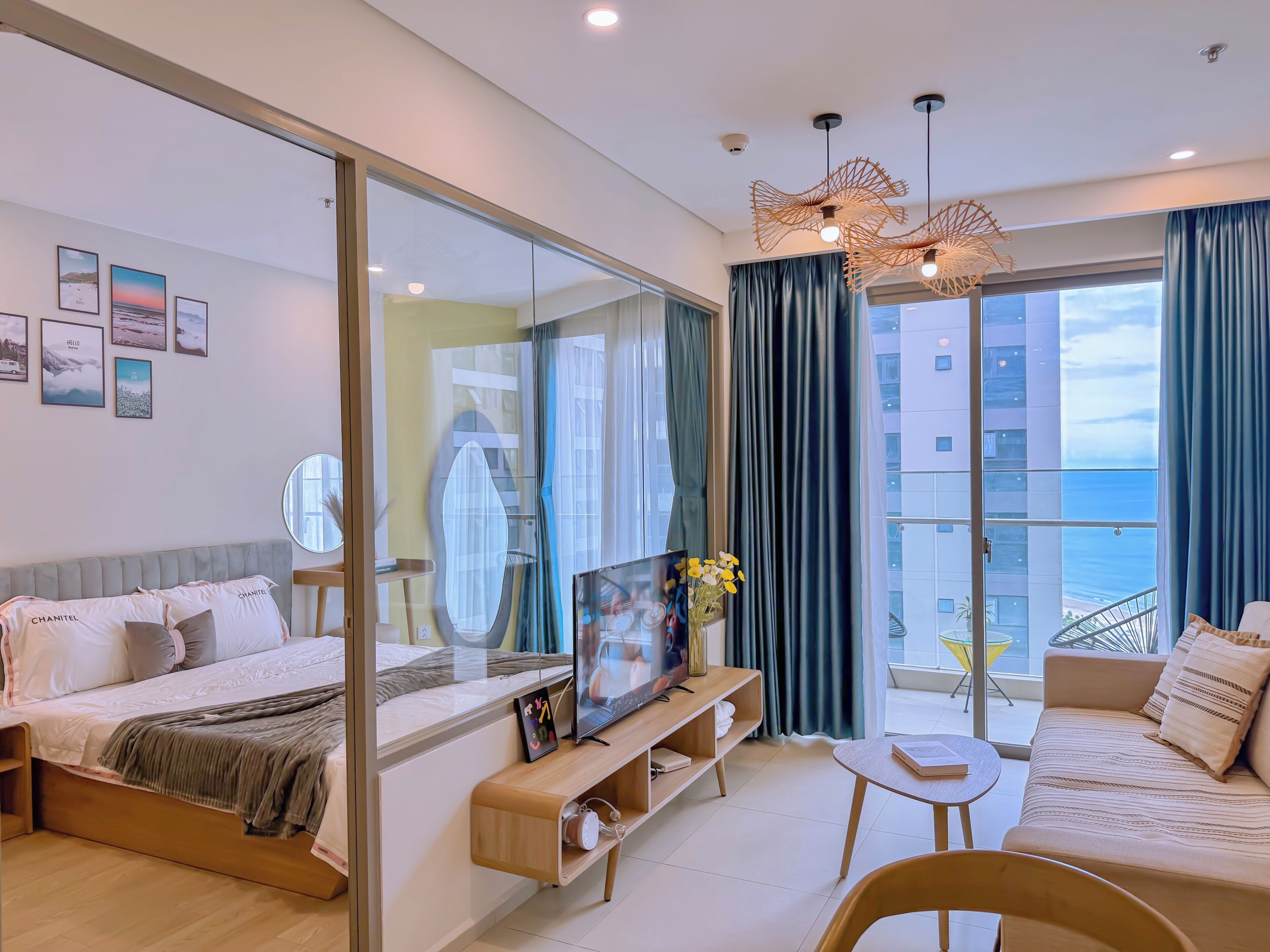 A modern hotel room with a bed, a sofa, a TV, a small table, and a balcony with a view.