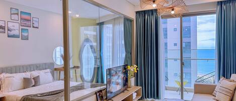 A modern hotel room with a bed, a sofa, a TV, a small table, and a balcony with a view.