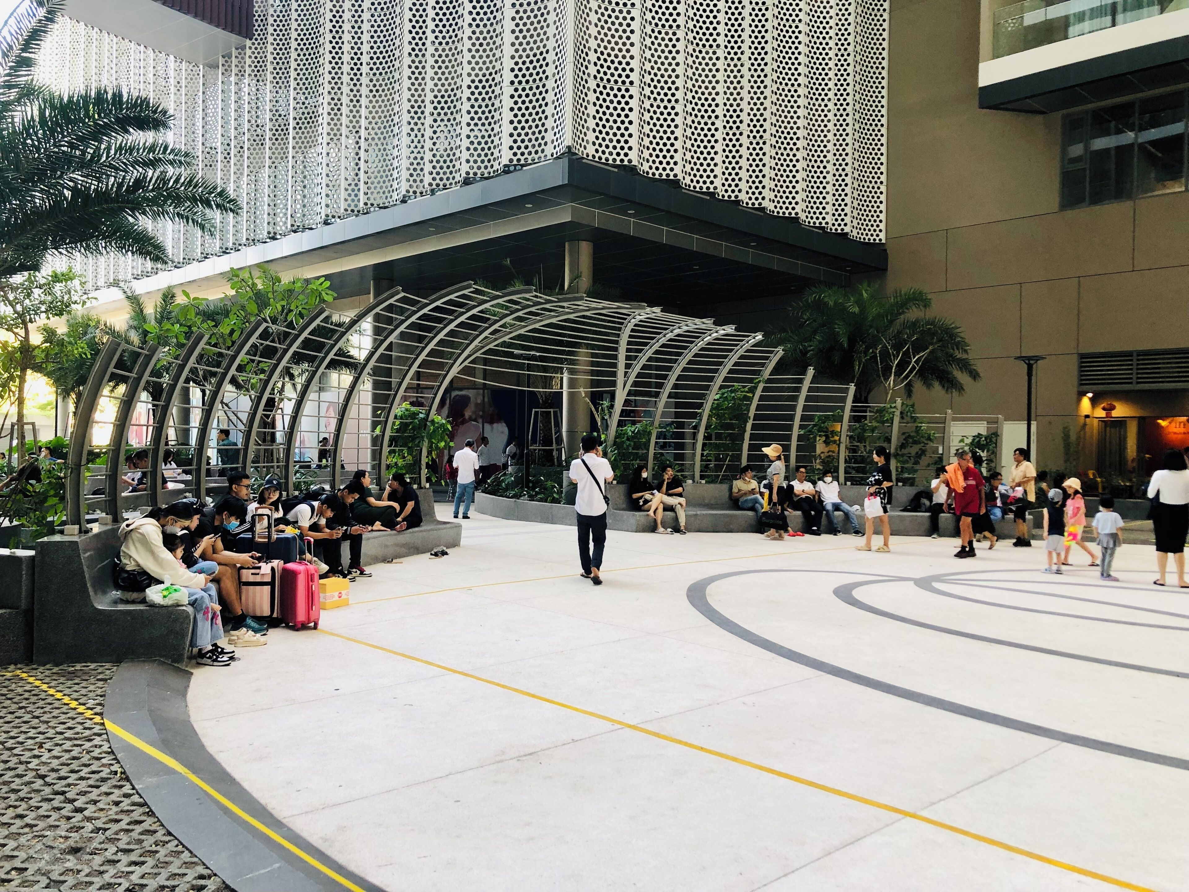 An outdoor public space with seating areas and a modern architectural design featuring a perforated metal facade and curved structures.