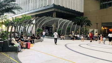 An outdoor public space with seating areas and a modern architectural design featuring a perforated metal facade and curved structures.