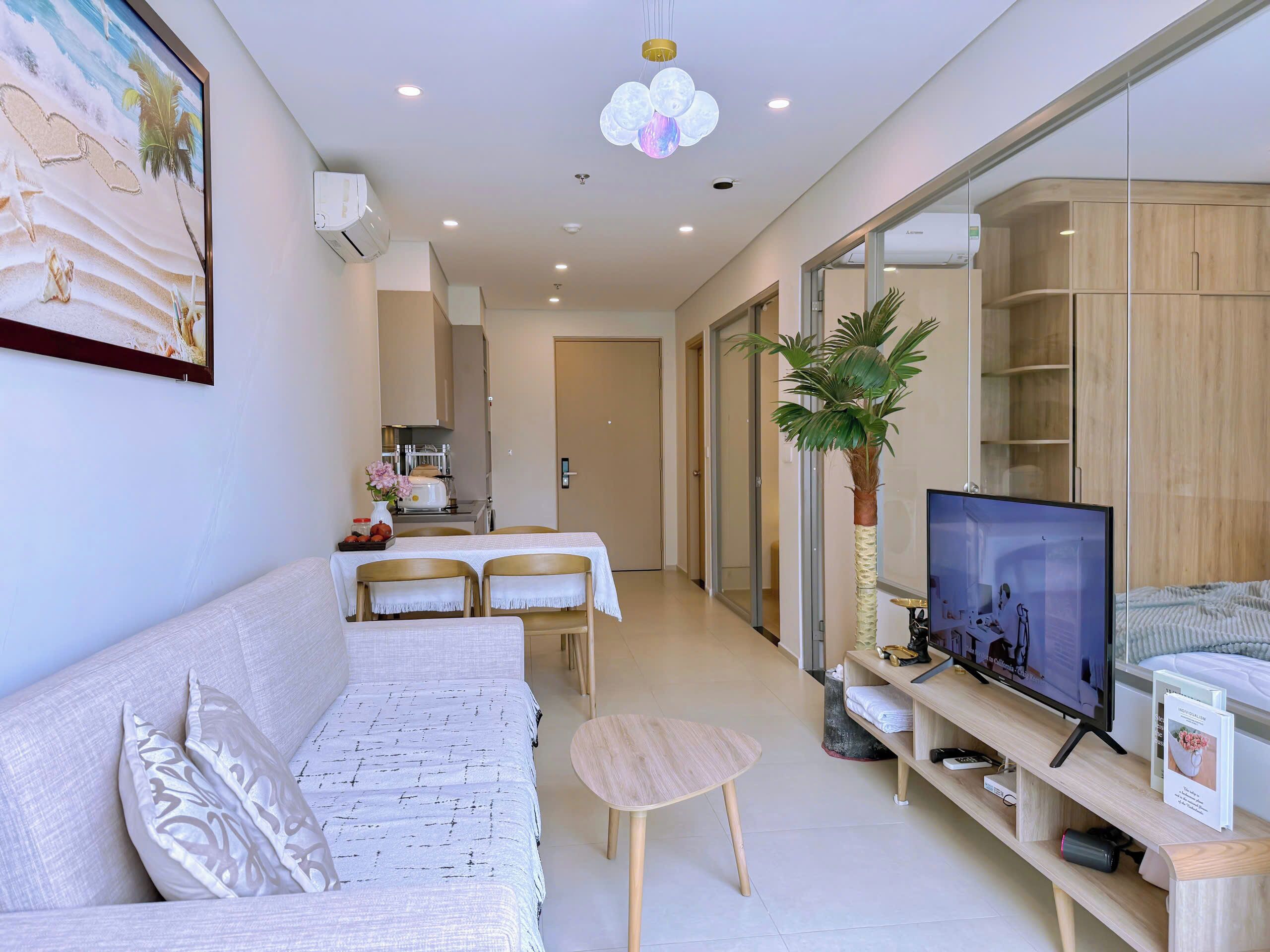 A modern living room with a sofa, a dining table, chairs, a TV, and a plant.