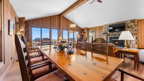 A spacious dining area with a wooden table and chairs, a fireplace, and a stone wall with a television. - Tiger Ridge, Single Level w/ Stunning Mtn Views (Highlands)
