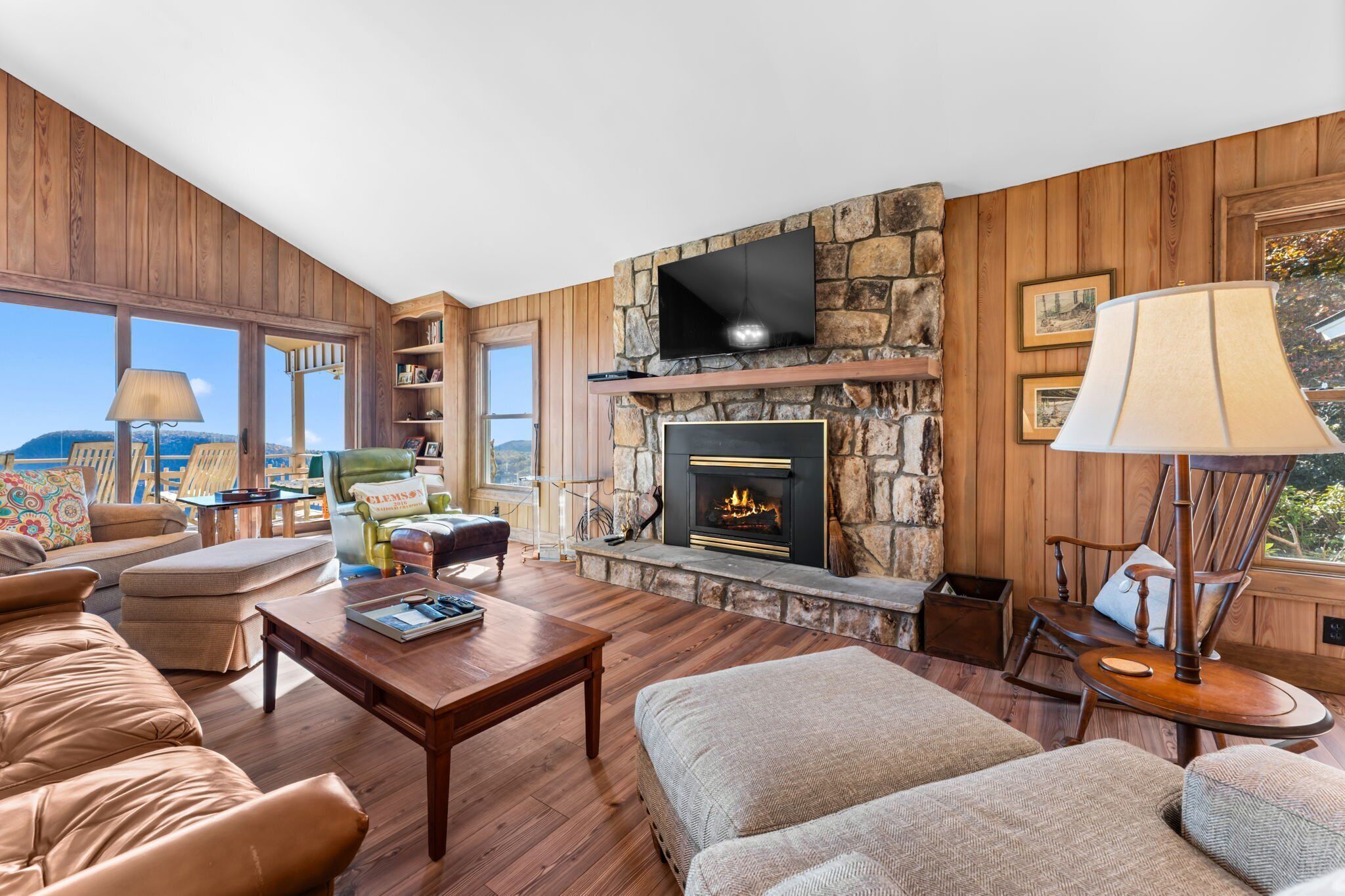 A cozy living room with a stone fireplace, wooden walls, a flat-screen TV, and comfortable seating.