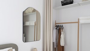 Ein Hotelzimmer mit Bett, Nachttisch mit Lampe, Spiegel, Kleiderschrank und Kleiderhaken.