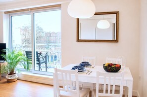 A dining area with a table set for two, a potted plant, and a view through a large window. - Notting Hill Views (London)