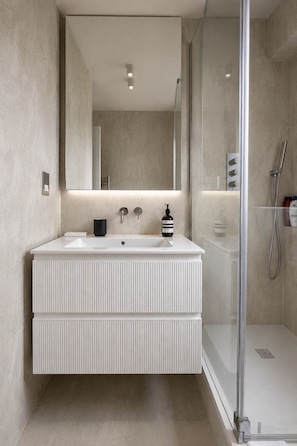 A modern bathroom with a large mirror, a white vanity, a shower enclosure, and a glass shower door. - Notting Hill Views (London)