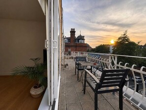 A balcony with a view of a building with a dome and chimney, outdoor furniture, and a potted plant. - Notting Hill Views (London)