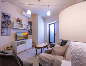 A living room with a TV, white shelves, a sofa, a coffee table, and artwork on the walls.