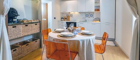 A compact kitchen with white cabinets, a dining table set for four, and wicker baskets on shelves.