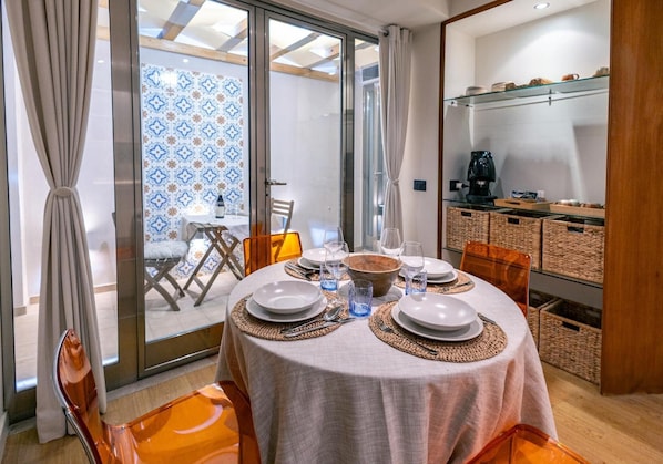 A dining area with a round table set for two, a coffee machine, and wicker baskets on shelves.