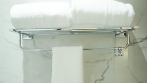 A bathroom with a marble wall, a towel rack holding two folded towels, and a single towel hanging from the rack. - Hotel Pacific Primee (Zirakpur)
