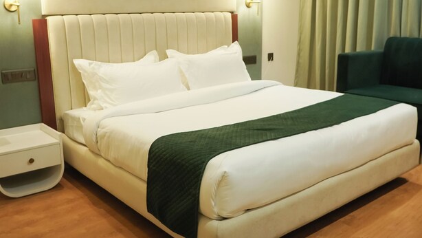 A hotel room with a large bed, a bedside table, a green sofa, and a window with curtains. - Hotel Pacific Primee (Zirakpur)
