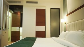 A hotel room with a bed, a wardrobe, a mirror, and a wall-mounted light fixture. - Hotel Pacific Primee (Zirakpur)
