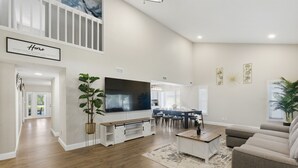 A spacious living room with a large TV, wooden flooring, and a comfortable sofa. - Levine's Spacious Clearwater Retreat with Pool (Clearwater)