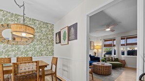 Un comedor con una mesa y sillas de madera, una lámpara colgante y un papel tapiz con estampado de hojas.
