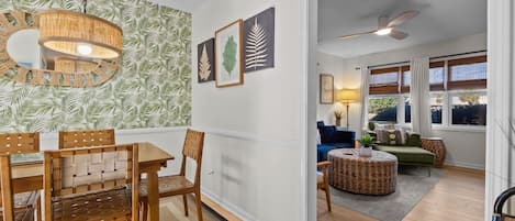 A dining area with a wooden table and chairs, a hanging light fixture, and a wall with a leafy wallpaper pattern.