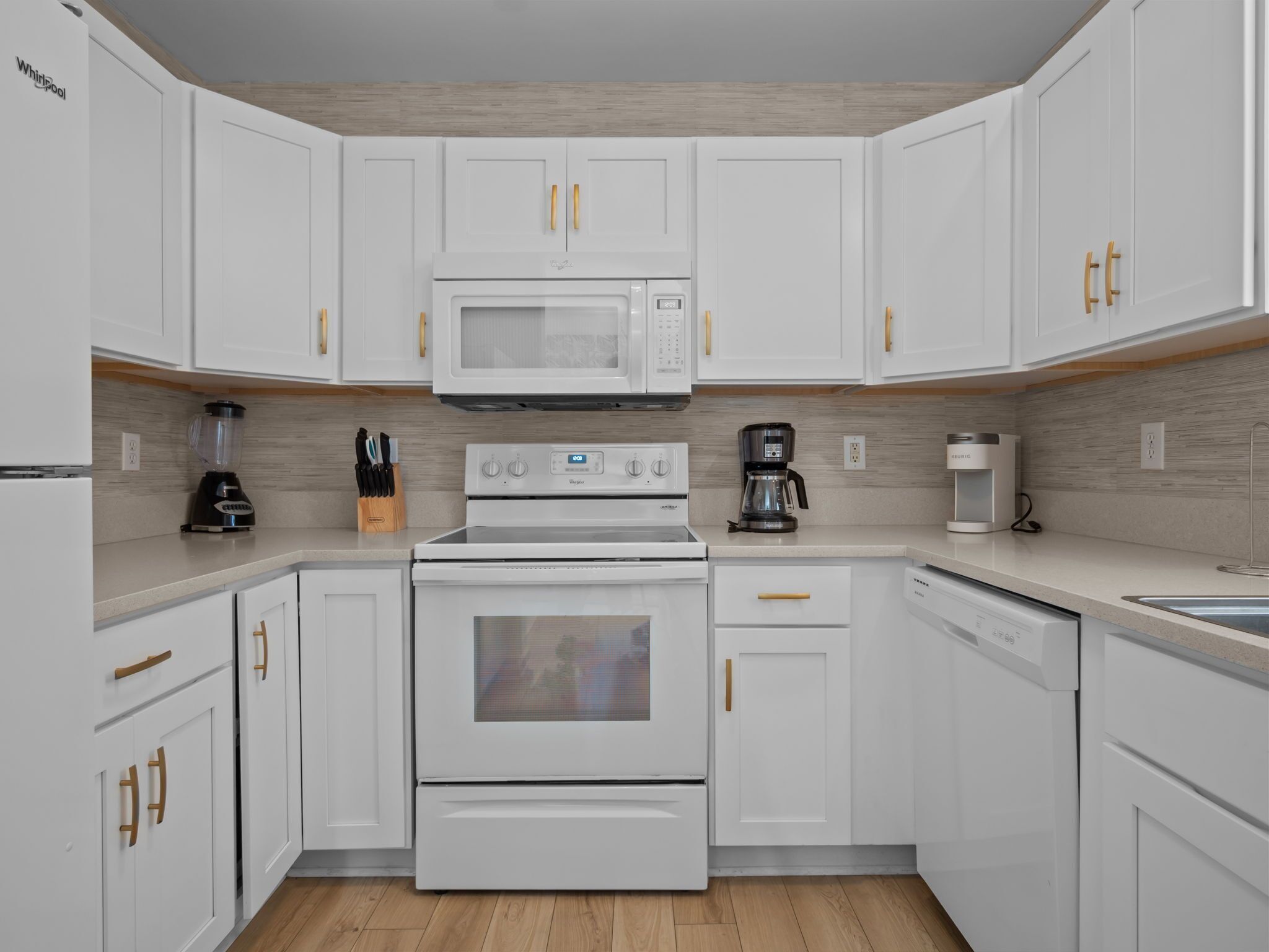 A modern kitchen with white cabinetry, a built-in microwave, a stove, and a coffee maker.