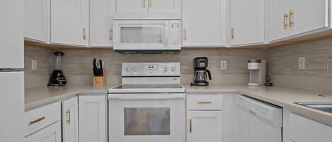 A modern kitchen with white cabinetry, a built-in microwave, a stove, and a coffee maker.