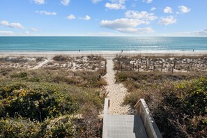 Un sentiero sulla spiaggia che conduce all'oceano, con cielo sereno.