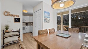 Un comedor amplio con una mesa y sillas de madera, una cocina al fondo y un ventanal con vistas al exterior.