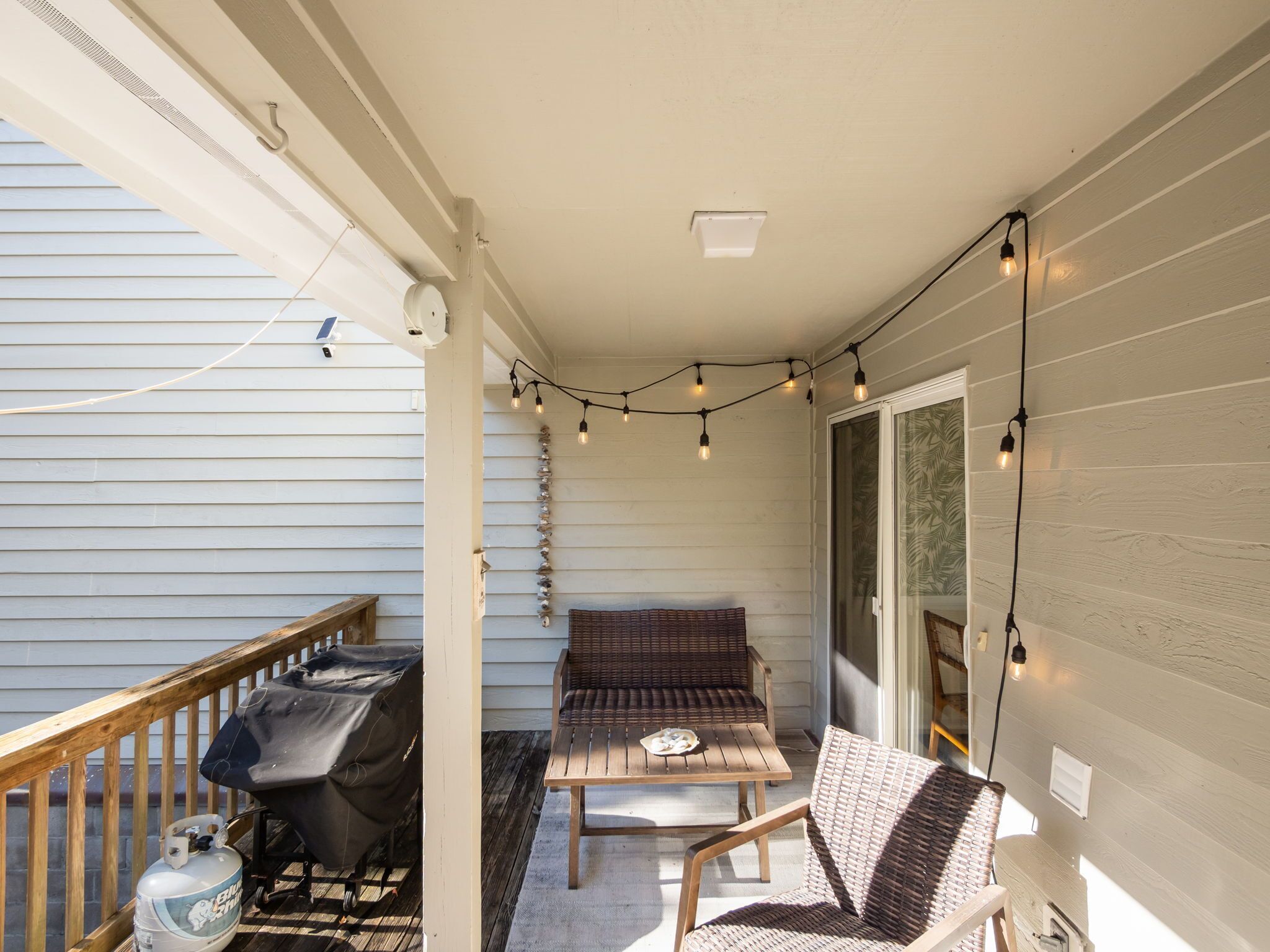 Een overdekt terras met een barbecue, zitplaatsen buiten en sfeerverlichting.