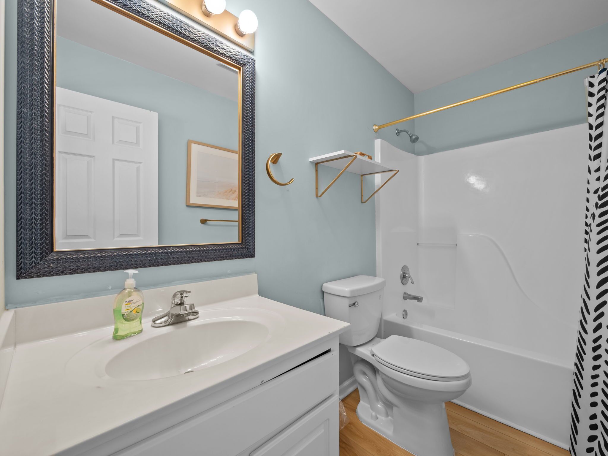 A bathroom with a white sink, a toilet, and a bathtub. There is a mirror with lights above it, and a towel rack.