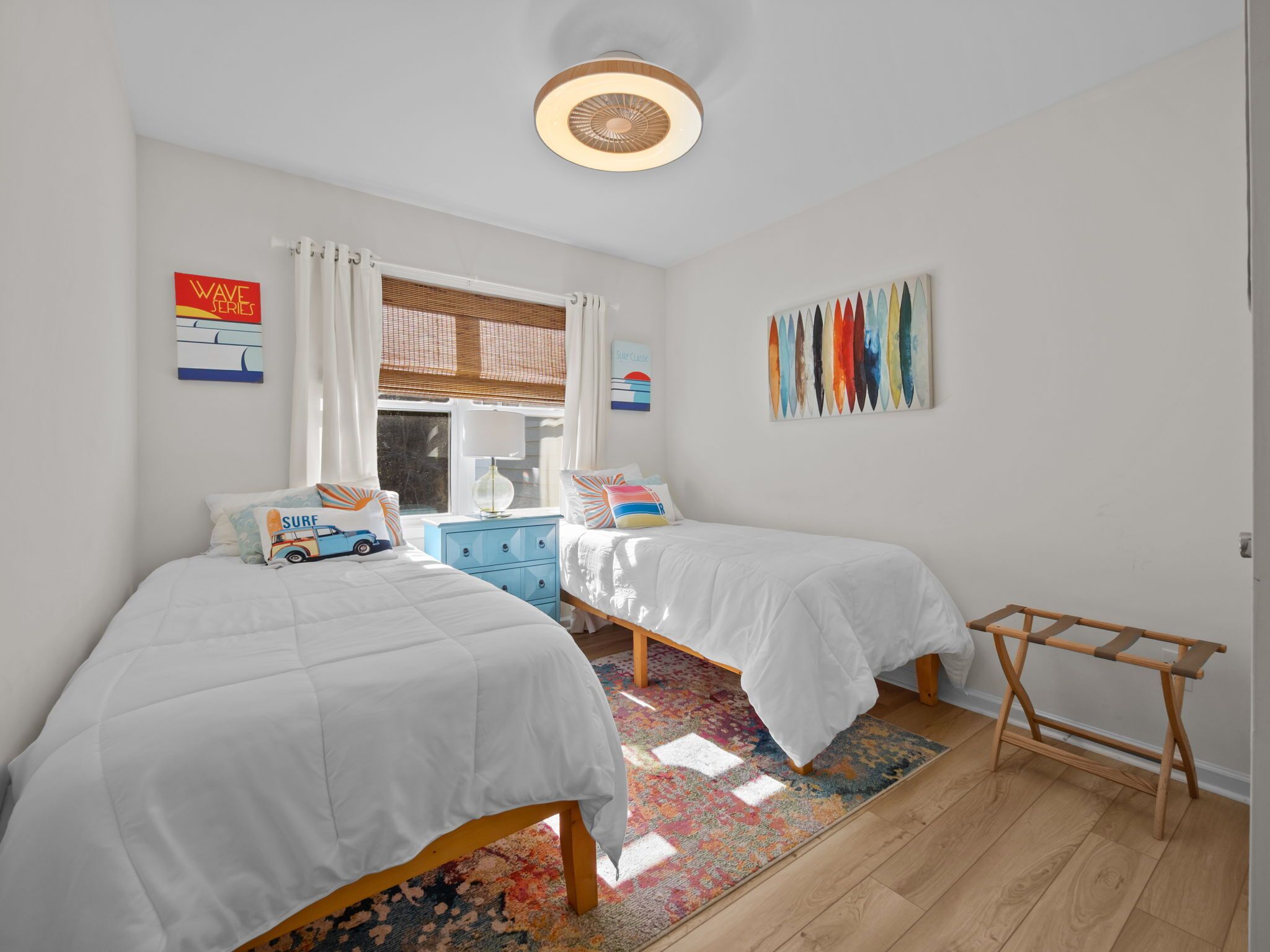 Une chambre avec deux lits, un tapis coloré, un plancher en bois et un ventilateur de plafond.