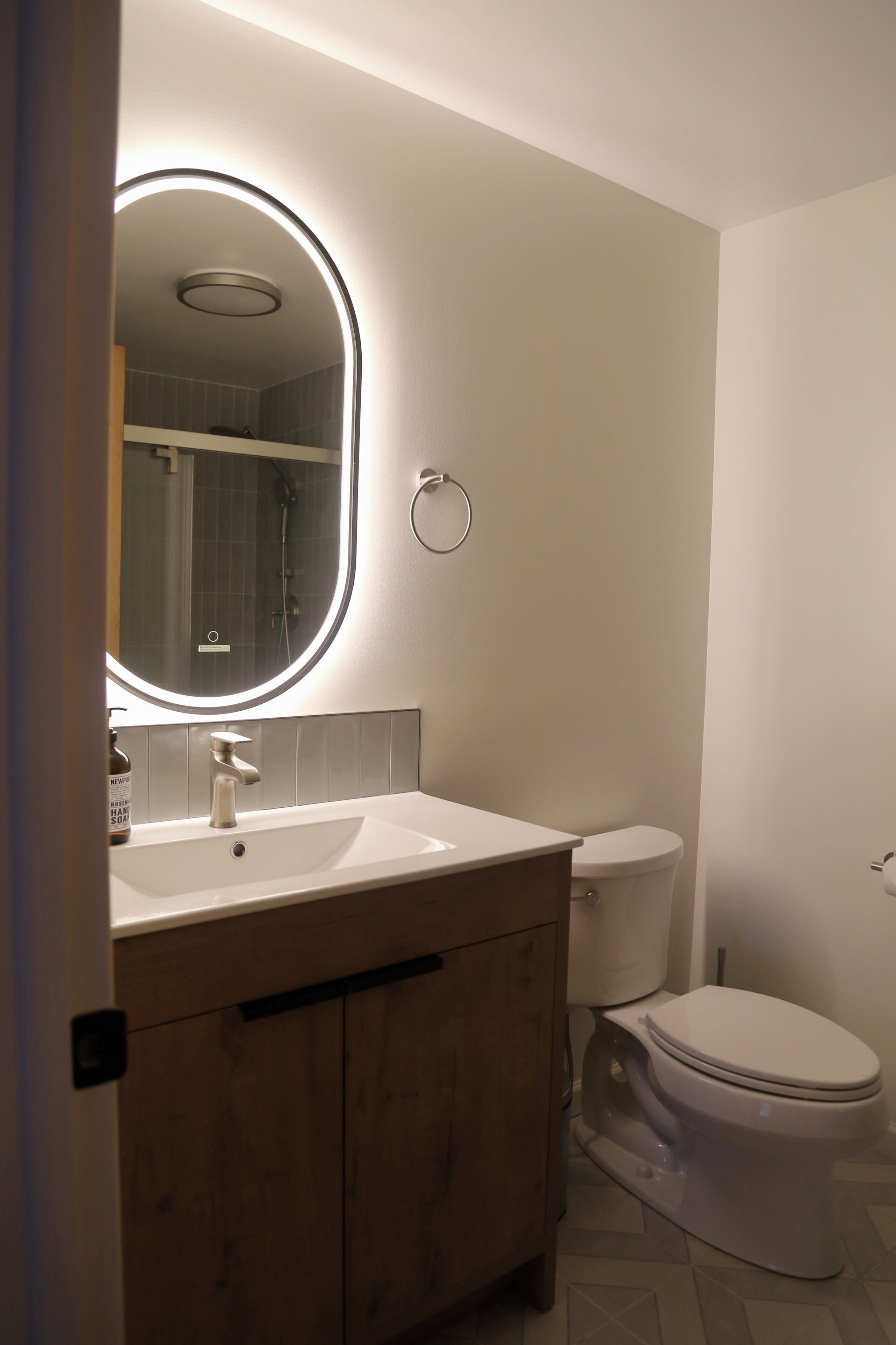 Et badeværelse med en hvid vask, et spejl med cirkulær belysning, et toilet og træskabe.