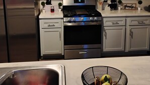 Une cuisine moderne dotée d’appareils électroménagers en acier inoxydable, de meubles blancs et d’un saladier de fruits posé sur le comptoir.