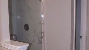 Une salle de bain avec une douche à parois de verre, un lavabo blanc et un sol en marbre.
