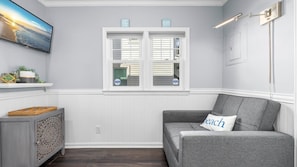 A room with a gray couch, a television on the wall, and a window with shutters. - Modern 2BR Close to Beach - Great Outdoor Space (Ocean City)