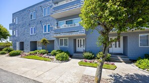 A multi-story residential building with a blue exterior, a small front garden, and a tree in the foreground. - Beach Block 4BR Townhouse w/ Beach Views & Parking (Ocean City)