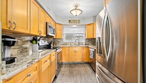 A kitchen with wooden cabinets, stainless steel appliances, a granite countertop, and a window with blinds. - Beach Block 4BR Townhouse w/ Beach Views & Parking (Ocean City)