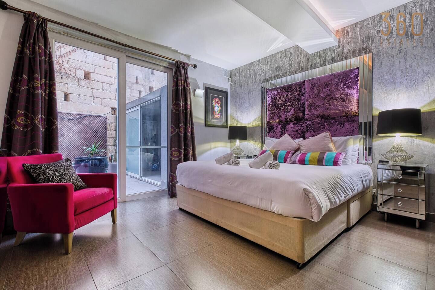 A modern bedroom with a large bed, a red armchair, and a glass door leading to an outdoor area.