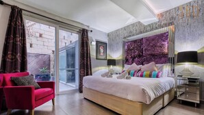 A modern bedroom with a large bed, a red armchair, and a glass door leading to an outdoor area. - Sea-View Terrace Maisonette, steps from Paceville! (Swieqi)