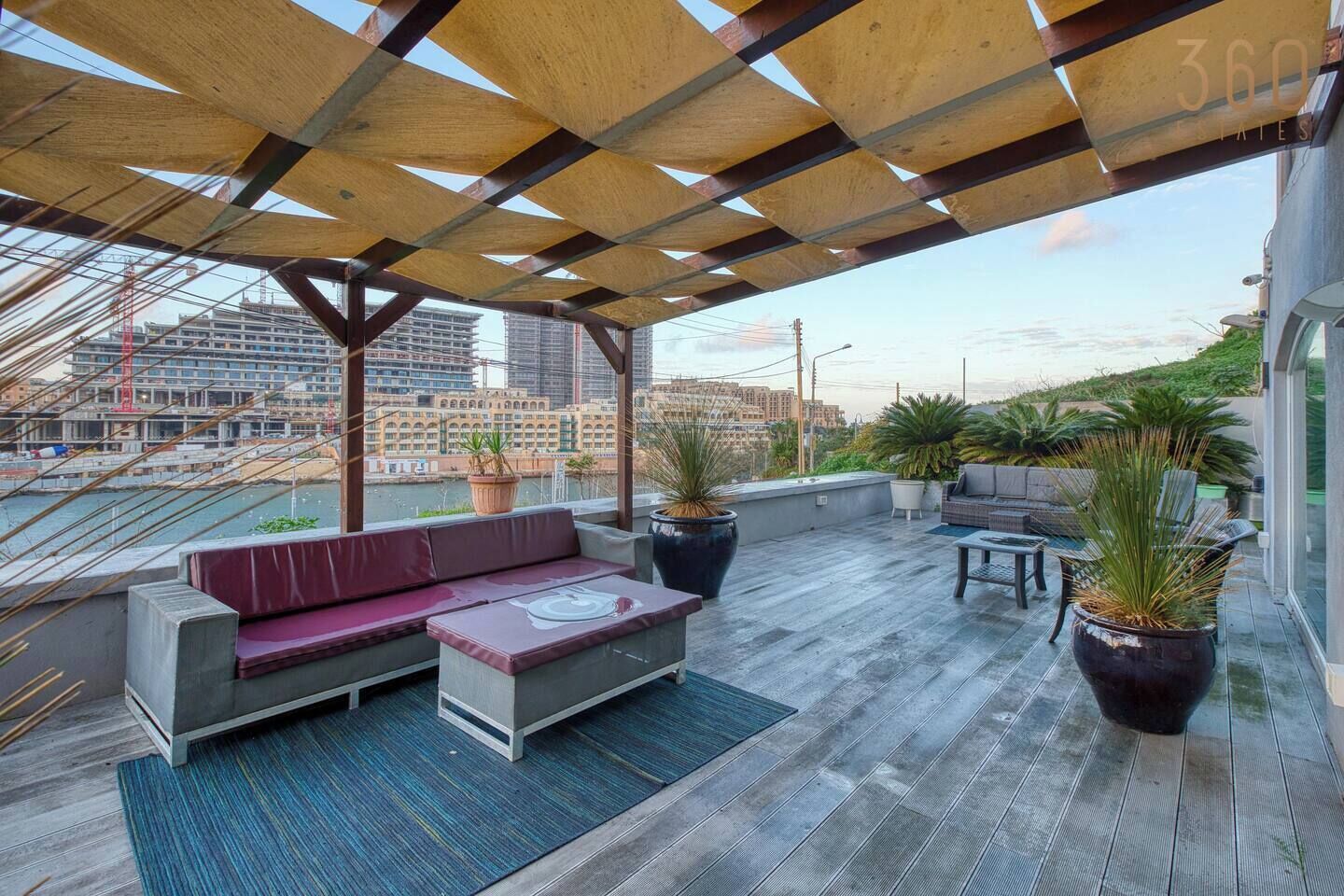 A rooftop terrace with a wooden pergola, seating area, and potted plants.