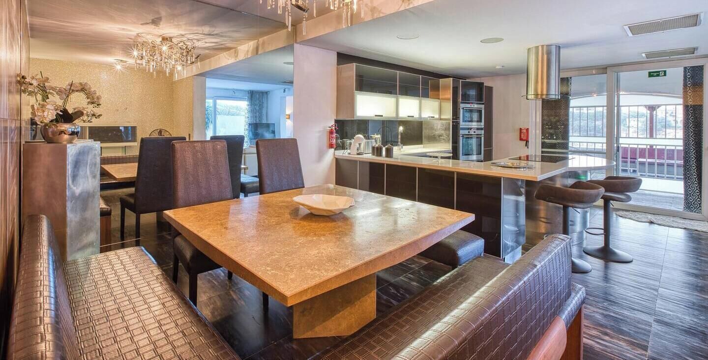 A modern dining area with a marble table, cushioned benches, and a chandelier.