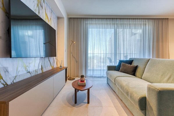 A modern living room with a sofa, a coffee table, and a TV mounted on a marble wall. - Elegant City Living with Terrace, Mercury Suites! (St. Julian`s)