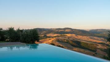 Une piscine offrant une vue sur des collines verdoyantes et un ciel dégagé.
