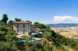 Una casa a due piani con piscina, immersa nel verde e affacciata su un paesaggio collinare.