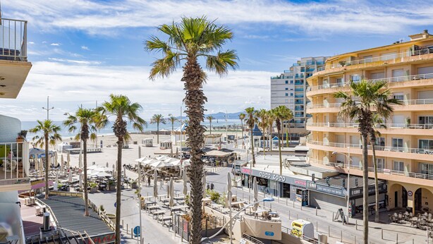 A coastal urban area with palm trees, a beach, and multi-story buildings. - Exceptional location, stunning sea view. Modern 48 m² apartment, center, 17 m² terrace. (Canet Plage)