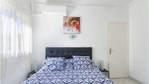 A bedroom with a bed, a painting, a door, and a window with curtains. - Exceptional location, stunning sea view. Modern 48 m² apartment, center, 17 m² terrace. (Canet Plage)