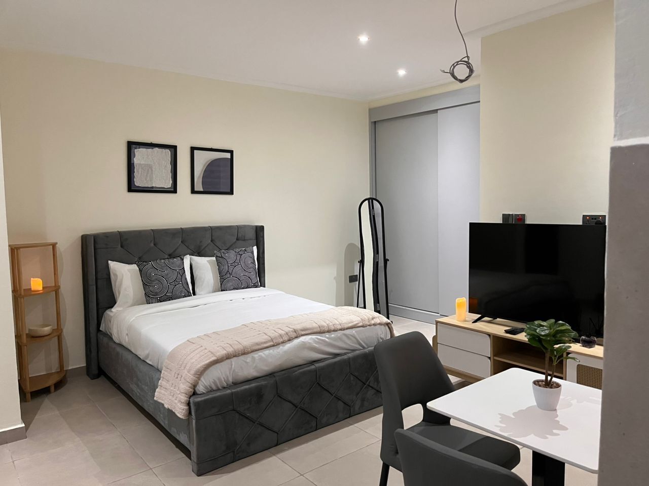 Een moderne slaapkamer met een bed, nachtkastje, stoel, televisie en een kleine plant.
