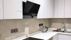 Una cocina moderna con armarios blancos, una placa de inducción negra, una cafetera de vidrio y un lavamanos de acero inoxidable.