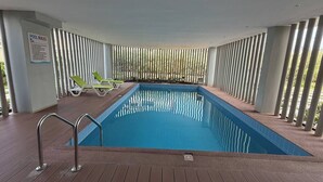 Una piscina con cubierta de madera, barandales metálicos y sillas de descanso verdes.