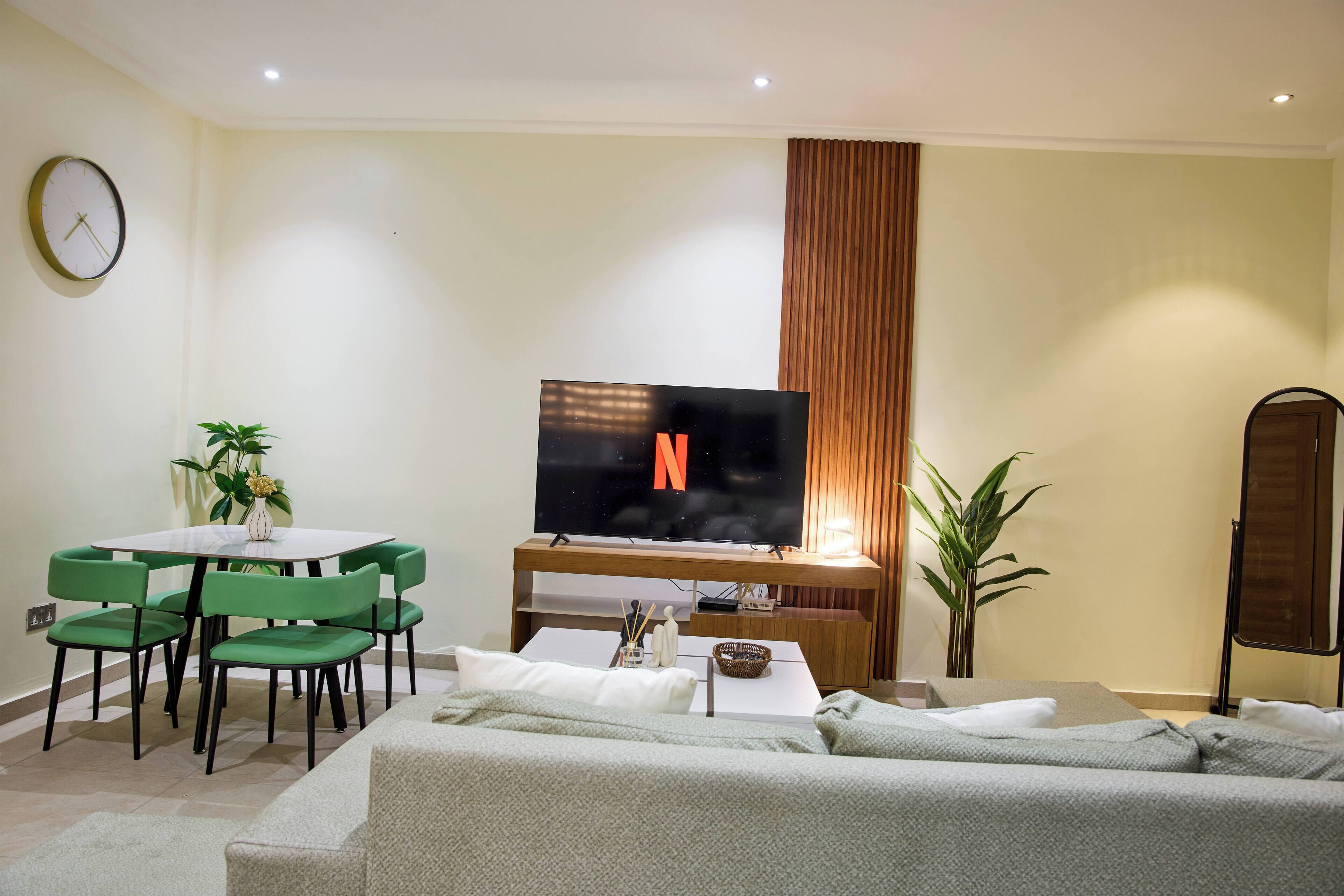 A living room with a TV, green chairs, a sofa, and a dining table.