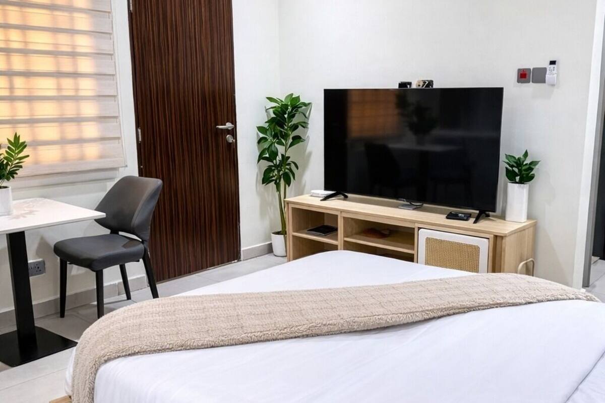 Un dormitorio con cama, televisor, escritorio y dos plantas en macetas.