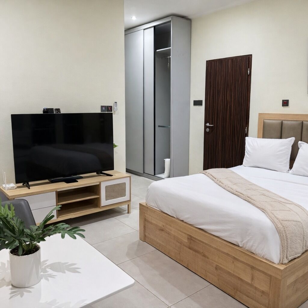 Une chambre d’hôtel moderne équipée d’un lit, d’une télévision, d’une armoire et d’une petite table agrémentée d’une plante.