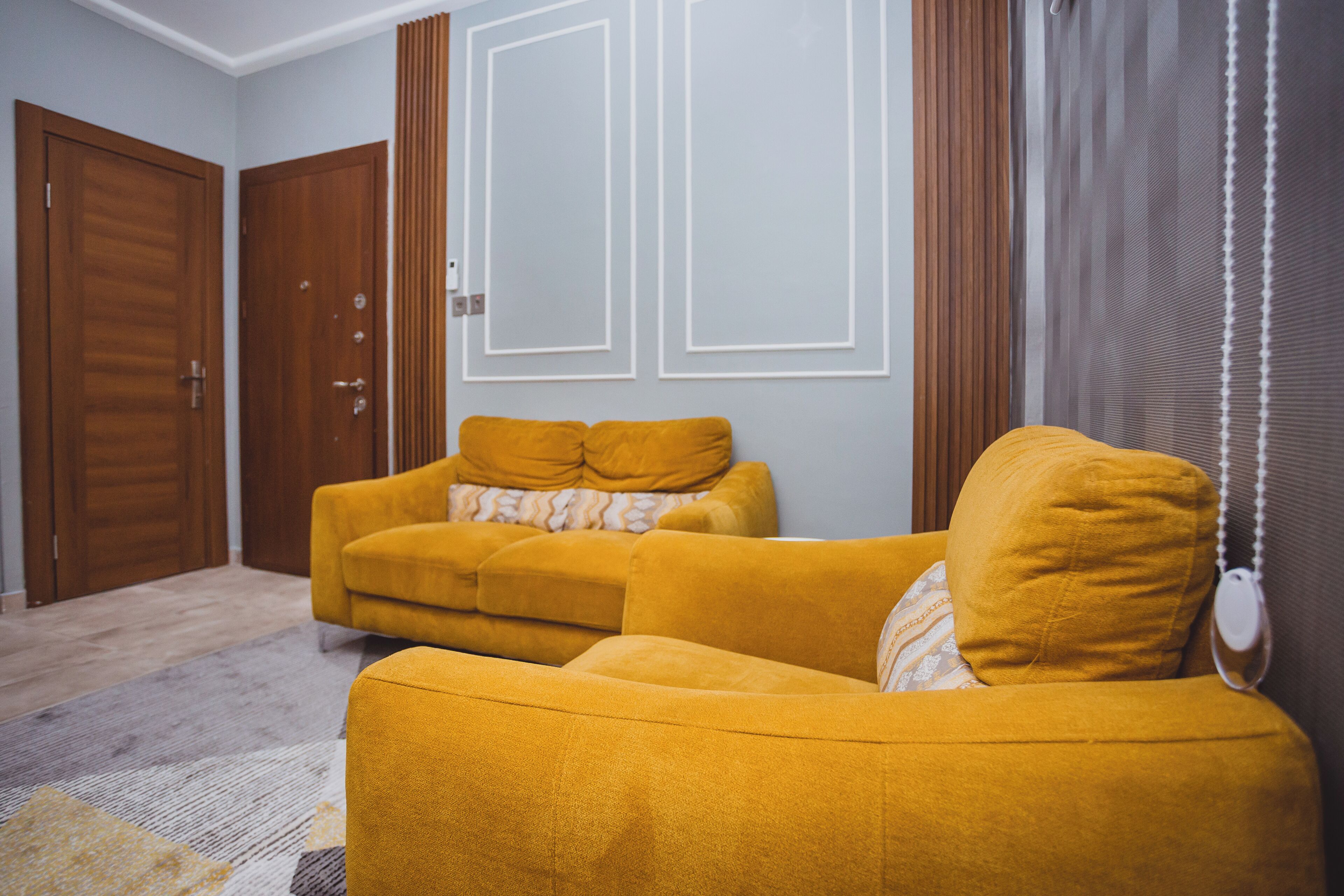 Ein Wohnzimmer mit einer Couch, einer Tür und einem fensterförmigen Aussparung mit Vorhängen.